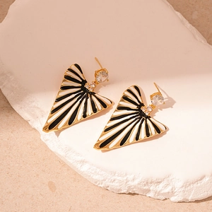 Macro shot of striped enamel earrings with gold edges on white stone surface