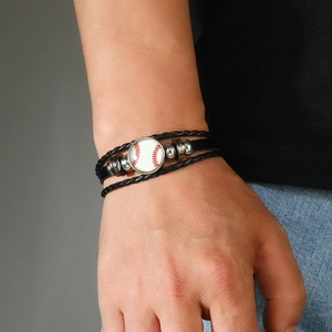 Détail du bracelet multicouche en cuir noir avec breloque baseball porté au poignet