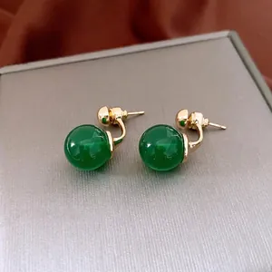 Retro style green sphere stud earrings with gold finish on a brushed metal background