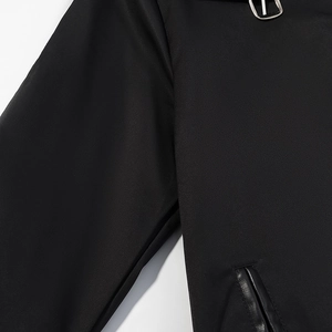 Detail of black trench coat featuring PU leather piping on pocket and metal D-ring accent