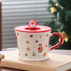 Detail of Santa Claus ceramic mug with red lid and festive patterns on a book