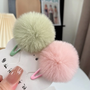 Close-up of fluffy faux rabbit fur pom pom hair clips in mint green and soft pink