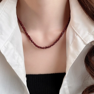Detail of dark red garnet beaded necklace layered on a crisp white shirt for a retro look