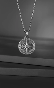 Detailed view of silver compass pendant with box chain on a textured grey background