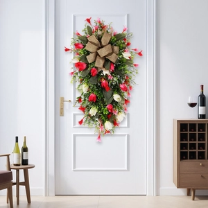 Teardrop Christmas swag with red flowers and a burlap bow hanging on a white door