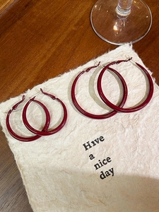Macro shot of two pairs of burgundy enamel hoop earrings on beige textured paper