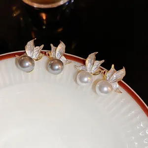 Elegant butterfly pearl stud earrings in gold and white enamel on a ceramic plate