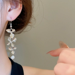 Close-up of silver flower drop earring with white pearl on model's ear in soft light