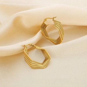 Irregular golden multilayer hexagonal earrings on beige silk fabric background