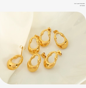 Detailed view of three pairs of irregular golden oval hollow earrings on a white ceramic plate