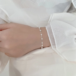 Primo piano del bracciale a sfere argentate indossato su tessuto bianco morbido