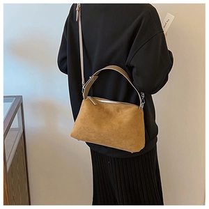 Detail of camel suede shoulder bag with dual straps worn by a model in black outfit