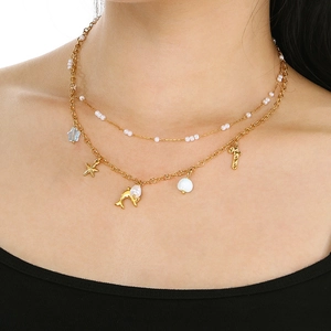 Detail of double-layer gold necklace with ocean charms and pearls worn by a model