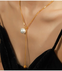 Detail einer vergoldeten Y-Kette mit elegantem weißen Perlenanhänger am Modelhals