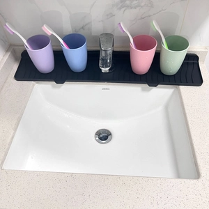 Top view of a black silicone faucet draining mat holding colorful cups on a bathroom sink