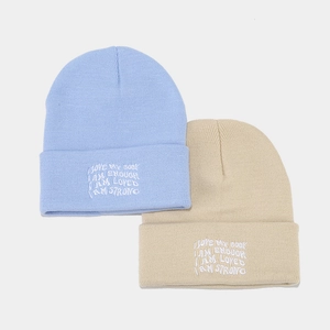 Detail of light blue and beige knit beanies with embroidered motivational quotes