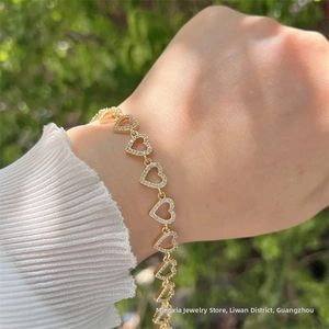 Detail of 18K gold heart-link bracelet with white zircons worn on wrist with white knit