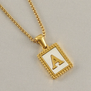 Detail einer quadratischen Goldkette mit dem Buchstaben A auf weißem Emaille