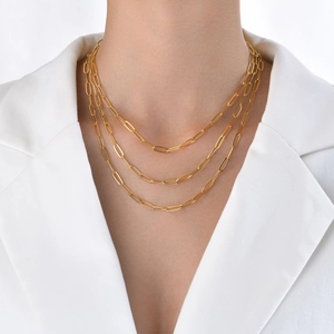 Three-layer golden paperclip chain necklace worn by a model in a white suit