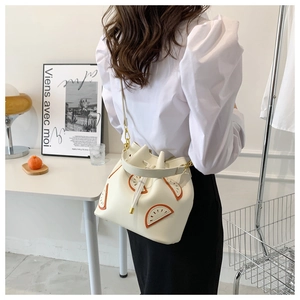 Detailed view of white bucket bag with orange fruit pattern and adjustable strap worn by model
