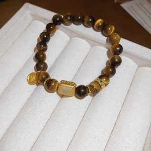 Macro detail of tiger eye stone beads bracelet with a gold hollowed gourd square pendant