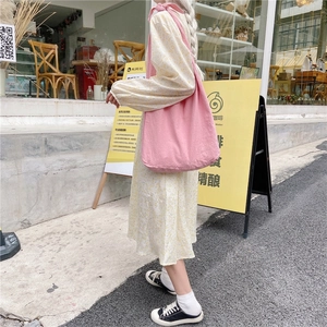 Pink canvas shoulder bag with adjustable bow straps in a casual outdoor setting