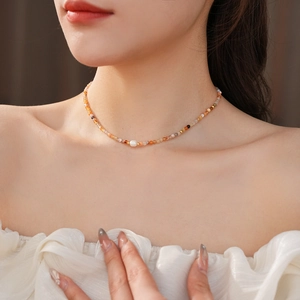 Detail of beaded necklace with freshwater pearl and warm-toned beads on neckline