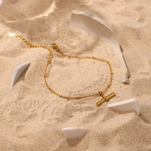 Close-up of gold titanium steel anklet with T-bar pendant on fine yellow sand