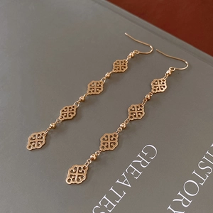 Macro detail of gold-tone dangle earrings with clover motifs on a grey book background