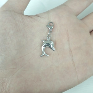 Macro shot of a silver dolphin pendant with lobster clasp held in a person's palm
