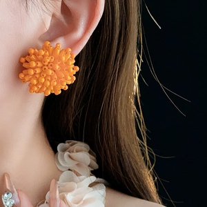 Close-up of bright orange handmade beaded flower earrings worn by a model