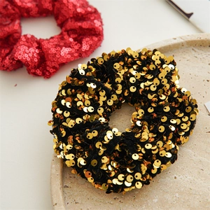 Close-up of sparkling gold sequin hair scrunchie on stone tray with red variant background