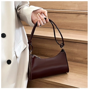 Detail of dark red glossy baguette bag featuring handcrafted knotted shoulder strap accents