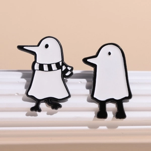 Cartoon black and white bird enamel pins set on a minimalist textured stone display stand