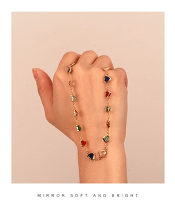 Close-up of golden necklace featuring colorful heart-shaped zircon stones on model hand