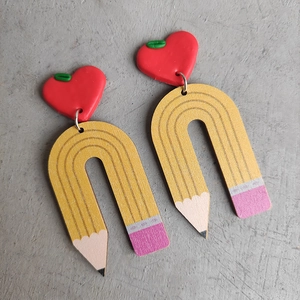 Close-up of creative pencil-shaped wooden earrings with red heart studs for teachers