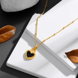 Golden bead chain necklace with black heart locket pendant on minimalist stone backdrop