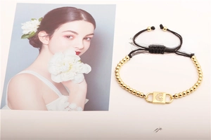 Detail of a braided bracelet featuring gold beads and a zircon-inlaid letter C charm