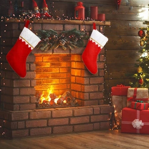 Detail of red and white Christmas stockings hanging on a brick fireplace with festive lights