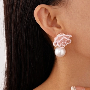 Detail of beaded pink flower earring with a large round pearl drop on female model