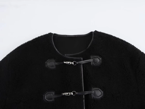 Gros plan sur un manteau en fourrure noire avec boucles métalliques et détails en cuir