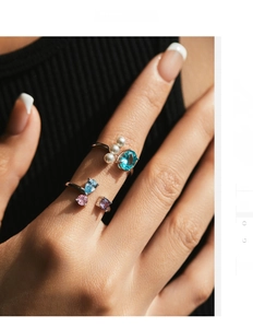 Detail of silver rings with blue crystals and pearls worn by a model on a dark background