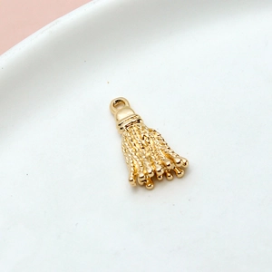 Macro shot of a shiny golden metal tassel pendant for DIY jewelry making on white ceramic
