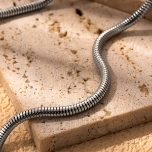 Minimalist silver stainless steel snake chain necklace on a marble textured stone surface