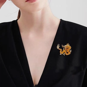 Detailed close-up of a golden dragon brooch featuring textured metal scales on a black suit