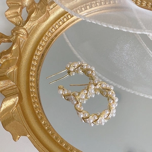 Detailed close-up of woven pearl hoop earrings on a vintage golden mirror background