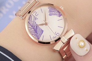 Close-up of rose gold watch featuring purple leaf patterns and bow-shaped mesh band