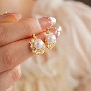 Detailed close-up of a gold feather earring with white pearl and sparkling zircons