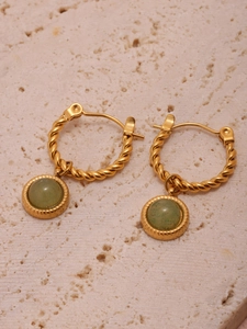 Detail of gold twisted hoop earrings with green agate stone charms on stone surface