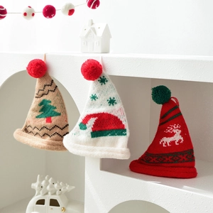 Three mini knitted Christmas hats with pom-poms for tree decor on a white shelf